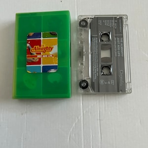 Könnte beinhalten: Ein grünes Kassetten-Etui mit einem gelben, roten und blauen Aufkleber, auf dem "Almighty Just Add Life" steht. Die Kassette befindet sich in einem durchsichtigen Plastik-Etui mit dem Text "The Almighty Just Add Life" und "Chrysalis" auf dem Etikett.