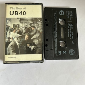 Puede incluir: Una cinta de casete negra con una etiqueta blanca. La etiqueta tiene el texto "UB40 - THE BEST OF UB40 VOLUME 1" y "Virgin Records".