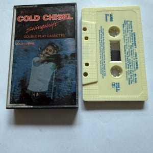 Op de afbeelding: Een vintage cassettebandje van het album "Swingshift" van Cold Chisel. De cassettecase is zwart met rode en witte tekst. De cassette zelf is lichtgeel van kleur. De albumtitel en de bandnaam staan prominent weergegeven.