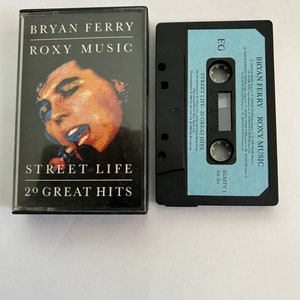 May include: A black cassette tape case with a blue label. The label has the text "BRYAN FERRY ROXY MUSIC STREET LIFE - 20 GREAT HITS" and "EGMTV 1 Side Two".