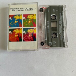 Può includere: Una musicassetta con una custodia in plastica trasparente e un'etichetta nera. L'etichetta riporta il testo "Everybody Wants to Shag... The Teardrop Explodes" e un elenco di titoli di canzoni. La musicassetta è una registrazione musicale.