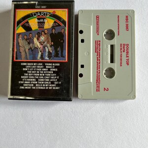 May include: A vintage cassette tape with a black and white image of a band on the front. The tape is labelled "Darts Double Top" and includes the song titles "Come Back My Love", "Young Blood", "Late Last Night", "Make It", "Don't Let It Fade Away", "Bones", "Too Hot In The Kitchen", "The Boy From New York City", "Daddy Cool", "The Girl Can't Help It", "It's Raining", "Sometime Lately", "Stay Away", "Get It", "Shotgun", "Bells In My Heart", and "Zing Went The Strings Of My Heart".
