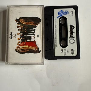 Puede incluir: Una cinta de casete negra con una etiqueta blanca. La etiqueta tiene el texto "stranglers 10" y el logotipo de Epic Records. La cinta de casete está en una caja de plástico transparente.