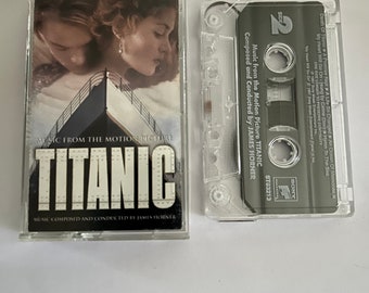 May include: Two clear cassette tapes. One cassette case features a movie still of a man and woman with the word "TITANIC" in large white letters. The other cassette shows the tape and the text "Music from the Motion Picture TITANIC".