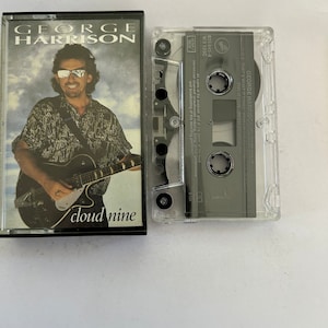 May include: A black cassette tape case featuring a photo of George Harrison playing a guitar. The text on the case reads "George Harrison" and "Cloud Nine".