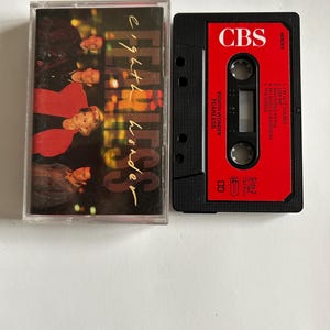 Puede incluir: Una cinta de casete roja con el título "Eighth Wonder Fearless" y el logotipo de CBS. La cinta de casete está en una caja de plástico transparente.