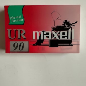 May include: A red and green cassette tape with the text "UR maxell 90" and "Normal Position" printed on it. The cassette tape features a graphic of a person sitting in a chair with a lamp.