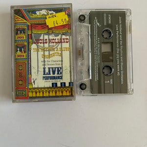 Könnte beinhalten: Eine Kassette mit einer Live-Aufnahme von Jools Holland und dem Rhythm and Blues Orchestra. Die Kassette befindet sich in einem durchsichtigen Plastikgehäuse mit einem schwarzen Etikett. Das Etikett trägt den Titel des Albums "Live Performance (the gig you were at)" und den Namen des Künstlers "Jools Holland and the Rhythm and Blues Orchestra".