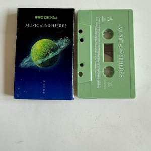 May include: A cassette tape and its case are displayed. The case is black with the text "MUSIC of the SPHERES" and a green planet graphic. The cassette is light green with the same text.