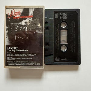May include: A vintage cassette tape of Levert's album "The Big Throwdown." The cassette case is clear with a black and white album cover featuring the band. The black cassette tape has the album title and song titles printed on it.