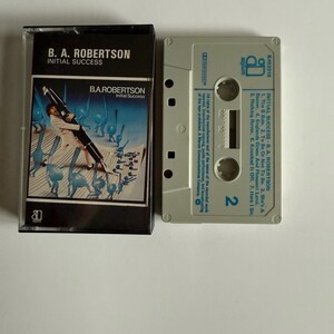 Puede incluir: Una cinta de casete con una foto en blanco y negro de un hombre tocando el saxofón. La caja está etiquetada como "B.A. Robertson Initial Success". La cinta de casete está etiquetada como "Initial Success - B.A. Robertson" y tiene el logotipo de Asylum Records.