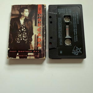 May include: A Jon Secada Just Another Day cassette single with its original cardboard sleeve. The sleeve features a portrait of the artist and the text Just Another Day. The black plastic cassette tape displays the tracklist and artist name.