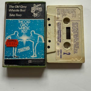 May include: A vintage cassette tape of "The Old Grey Whistle Test - Take Two." The cassette case is green and features a blue and white design with the text "The Old Grey Whistle Test" and "Take Two." The cassette itself is beige with black text.