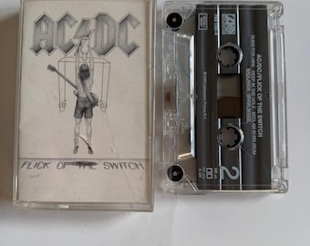 May include: A cassette tape of the album "Flick of the Switch" by AC/DC. The album cover features a black and white illustration of a person holding a guitar.