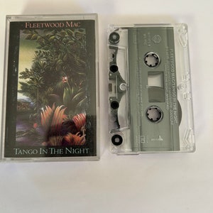May include: A cassette tape of Fleetwood Mac's album "Tango in the Night". The album cover features a lush, tropical jungle scene with vibrant green foliage and red flowers. The cassette tape is clear plastic with a black label.