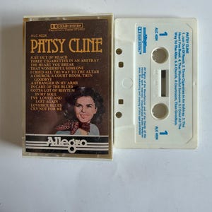 Op de afbeelding: Een witte cassettebanddoos met een zwart en bruin inzetstuk. Het inzetstuk bevat een foto van Patsy Cline en de titel "Patsy Cline" in grote, vetgedrukte letters. De tekst "ALC 4024" staat in de linkerbovenhoek van het inzetstuk. Het inzetstuk vermeldt de nummers op de cassetteband: "Just Out of Reach", "Three Cigarettes in an Ashtray", "The Heart You Break", "That Wonderful Someone", "I Cried All the Way to the Altar", "A Church, A Courtroom, Then Goodbye", "A Stranger in My Arms", "In Care of the Blues", "Gotta Lot of Rhythm in My Soul", "I've Loved and Lost Again", "Lovesick Blues", "Cry Not for Me".
