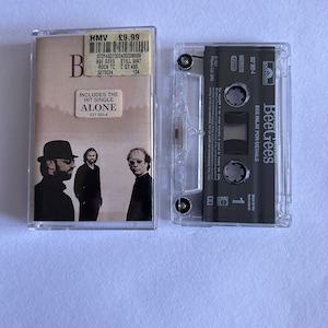 Puede incluir: Una cinta de casete transparente con la portada del álbum de los Bee Gees. La portada presenta una imagen en tonos sepia de los miembros de la banda. La cinta de casete lleva la etiqueta "STILL WAT" e incluye el sencillo "ALONE".
