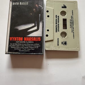 以下が含まれることがあります： Wynton MarsalisのアルバムHot House Flowersのカセットテープとプラスチックケース。ケースの表紙にはミュージシャンのモノクロ写真とWynton Marsalis Hot House Flowersの文字が印刷されている。ベージュ色のカセット本体には黒い文字のラベルが貼られている。