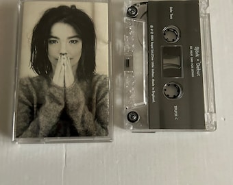 May include: A cassette tape case with a black and white photo of Björk on the front. The case is clear plastic and the tape is labeled "Björk - Debut".