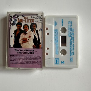 以下が含まれることがあります： 黒いラベルが付いた白いカセットテープ。ラベルには「The Very Best Of... The Chi-Lites」というテキストと、各面の曲名が記載されています。カセットテープは透明なプラスチックケースに入っています。