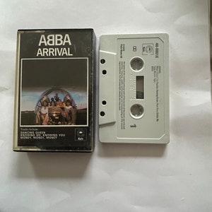 以下が含まれることがあります： 黒いカセットテープケースに「ABBA Arrival」のタイトルと、前面にバンドの写真が印刷されています。ケースの裏面には、「Dancing Queen」、「Knowing Me, Knowing You」、「Money, Money, Money」の曲が記載されています。