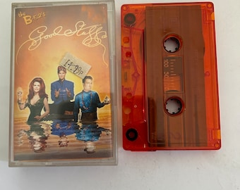 May include: A cassette tape of The B-52's album "Good Stuff" with a price tag of £7.99. The cassette tape is orange and has a clear plastic case. The album cover features a band photo with a yellow, orange, and red background.
