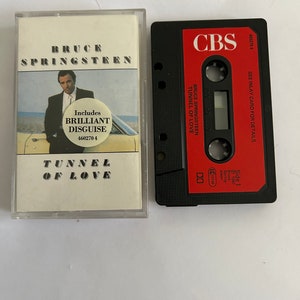 May include: A black cassette tape with a red label that says "CBS" and "Bruce Springsteen Tunnel of Love". The cassette tape is in a clear plastic case with a white label that says "Bruce Springsteen" and "Tunnel of Love". The label also includes a smaller red circle that says "Includes Brilliant Disguise 460270 4".