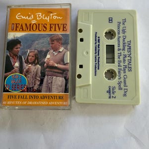 Puede incluir: Un casete de audio y su estuche. El estuche presenta el texto "Enid Blyton The Famous Five" y una foto de tres niños. El casete es de color verde claro y tiene el texto "TAPES'N'TALES" y "The Ugly Duckling - Pluto Plays Guard Dog".