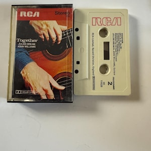 Puede incluir: Una cinta de casete de audio vintage del álbum "Together" de Julian Bream y John Williams. La caja del casete presenta una foto de manos tocando la guitarra. La cinta blanca tiene el logotipo de RCA y la información de la pista.