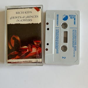 May include: A cassette tape with a white case and a blue label. The label says "TC-EMC 3263" and "RICH KIDS - GHOSTS OF PRINCES IN TOWERS". The tape is a vintage music cassette.