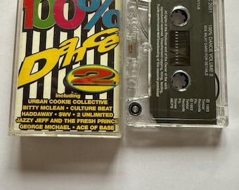 May include: A clear cassette tape case for "100% Dare 2" featuring 21 dance hits. The case is open, revealing the cassette tape. The cover is colorful and includes artist names such as George Michael and Ace of Base.