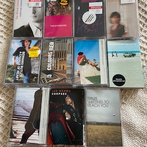 May include: A collection of nine cassette tapes, including music by Suede, Pulp, Bernard Butler, Ian Brown, and Travis. The tapes are arranged in three rows, with the titles and artists clearly visible. The tapes are all in clear plastic cases with colorful artwork.