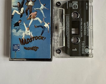 May include: A vintage cassette tape for the album "Madstock! Madness" by Madness. The cover features a blue background with band members in mid-air. The cassette case is clear, with the album title and track information visible.