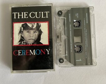 May include: A cassette tape of The Cult's album "Ceremony". The album cover features a black and white photo of a young person with a painted face. The text "The Cult" is in white letters on a black background. The text "Ceremony" is in red, blue, and white letters on a black background.