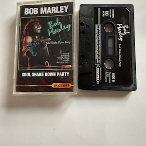 Könnte beinhalten: Eine Vintage-Kassette des Albums "Soul Shake Down Party" von Bob Marley. Das Kassettenetui zeigt ein Foto von Marley und Albumdetails. Die schwarze Kassette ist mit "Seite B" beschriftet. Ein Sammlerstück.