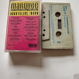 May include: A cassette tape and its clear plastic case. The insert features the text Marquee The Collection 1958-1983 Volume 1 with a list of artists including The Who, Rod Stewart, and Elton John on a pink background. The cassette is grey with blue text.