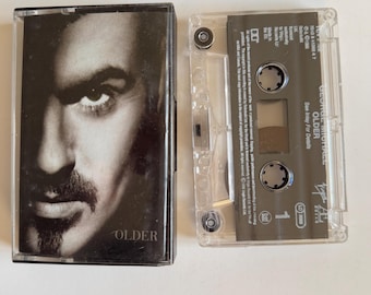 May include: A black cassette tape case with a black and white photo of George Michael on the front. The case has the title "OLDER" printed on it. The cassette tape is labeled "George Michael - OLDER" and has the song title "Too Funky" printed on it.
