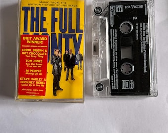 May include: A cassette tape of the soundtrack for the film "The Full Monty". The cassette tape is in a clear plastic case with a black label. The label has the title of the film, the record label, and the track list. The cassette tape is a physical media format for storing and playing audio recordings.