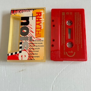 Peut inclure: Une cassette audio rouge et jaune avec le texte "Rhythm + Noise" et "Underground Magazine" imprimé dessus. La cassette audio présente une liste de groupes, dont Cabaret Voltaire, Depeche Mode, Throwing Muses, Sonic Youth, The Normal, Clock DVA, The Shamen et Lowlife.