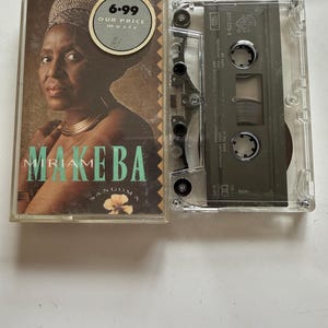 Könnte beinhalten: Eine Miriam Makeba Sangoma Musikkassette in einer transparenten Kunststoffhülle. Das Cover zeigt ein Porträt der Künstlerin, den Text "MIRIAM MAKEBA SANGOMA" und einen runden "6.99 OUR PRICE music" Aufkleber. Die Kassette selbst ist grau mit schwarzen Spulen.
