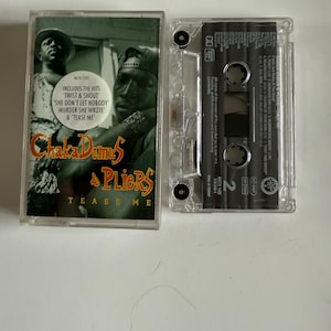 Könnte beinhalten: Eine transparente Kassette mit dem Albumcover von Chaka Demus & Pliers' "Tease Me". Das Cover zeigt ein grünes und schwarzes Bild der Künstler. Der Text enthält die Hits "Twist & Shout", "She Don't Let Nobody", "Murder She Wrote" und "Tease Me."