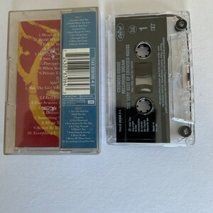 May include: A cassette tape with a clear plastic case and a black label. The label has the text "Crowded House Recurring Dream The Very Best of Crowded House" printed on it. The cassette tape is a music album.