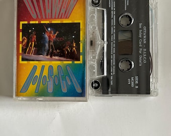 May include: A cassette tape with a clear plastic case. The front of the case has a colourful image of a band performing on stage. The text "OTTAWAN - D.I.S.C.O" is printed on the case. The back of the case has the text "See Inlay Card For Details" and "SIDE B MCJHD 079".
