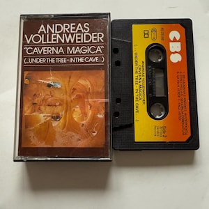 May include: A vintage cassette tape of Andreas Vollenweider's "Caverna Magica" album. The cassette case is brown with white text, and the tape itself is black with a yellow label. The album art features an illustration of a cave scene.