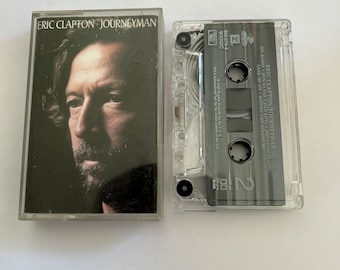Puede incluir: Una cinta de casete y una portada de álbum para el álbum Journeyman de Eric Clapton. La portada del álbum presenta una foto en blanco y negro de Eric Clapton. La cinta de casete es de plástico transparente con una etiqueta negra que dice "Eric Clapton/Journeyman" y enumera las canciones "No Alibis", "Run So Far", "Old Love", "Breaking Point", "Lead Me On" y "Before You Accuse Me".