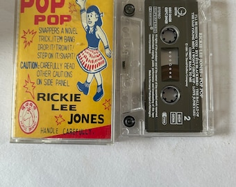 May include: A yellow and red cassette tape with the title "Pop Pop" and the artist "Rickie Lee Jones". The cassette tape features a cartoon illustration of a girl in a red skirt and blue top. The text "Handle Carefully" is printed on the cassette tape.