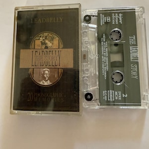 May include: A vintage cassette tape of "The Leadbelly Story" album. The cassette case is dark with gold lettering and a portrait. The tape itself is clear with green text. The album cover reads "20 Phonographic Memories."