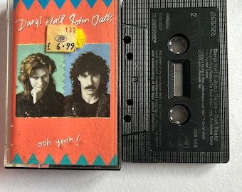 May include: A black cassette tape with the title "Daryl Hall & John Oates - Ooh Yeah!" and the band's name and album title printed on the label. The cassette tape is in a clear plastic case with a red, white, and blue design.
