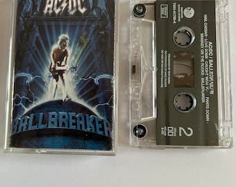 May include: A cassette tape of the album "Ballbreaker" by AC/DC. The album cover features a man in a black leather jacket and jeans standing in front of a blue and white background with the band's name and album title in white letters.