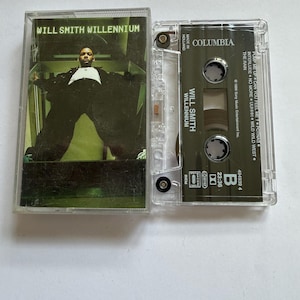 Puede incluir: Un estuche de cinta de casete transparente con el álbum "Willennium" de Will Smith. La portada muestra a Will Smith con un traje negro. La cinta de casete está etiquetada como "Columbia" e incluye la lista de canciones.